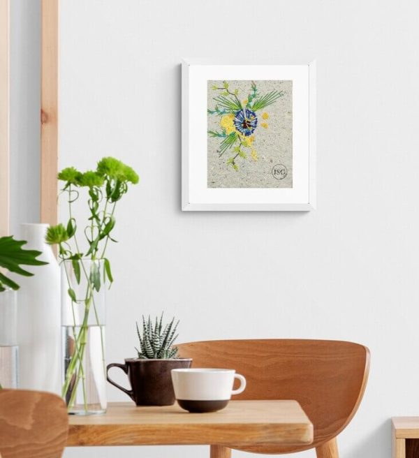 artwork of blue and yellow flowers created using embroidery on handmade paper displayed in a white frame in a dinning room