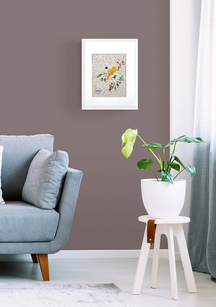 artwork of flowers and red berries embroidered on handmade paper desplayed in a living room framed in a white frame next to a blue couch