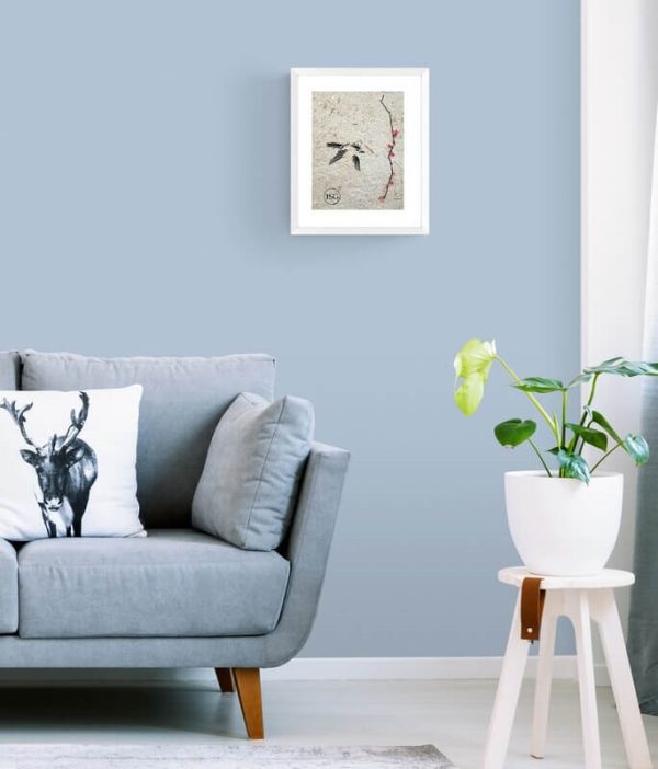 artwork of a bird flying through the air beside a tree branch with pink flower displayed in a white frame in a living room with a blue couch