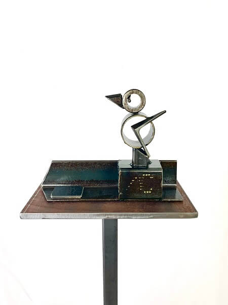 A metal sculpture of a gosling made from scrap pieces of metal displayed on a metal podium